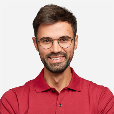 Man with short brown hair, beard, and glasses wearing a red polo shirt, smiling at the camera against a plain light background.
